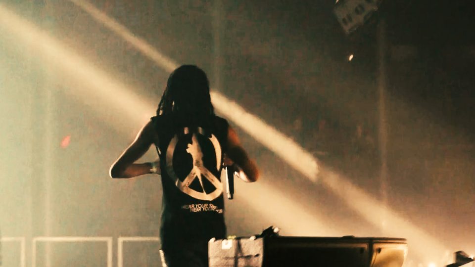 Che from behind, facing the light beams at the front of the stage