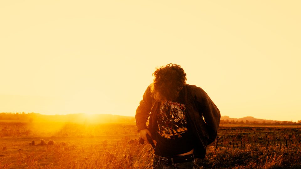Figure crouched in a field at golden hour, sun on the horizon, by Luca Barbieri (lucabrbi)