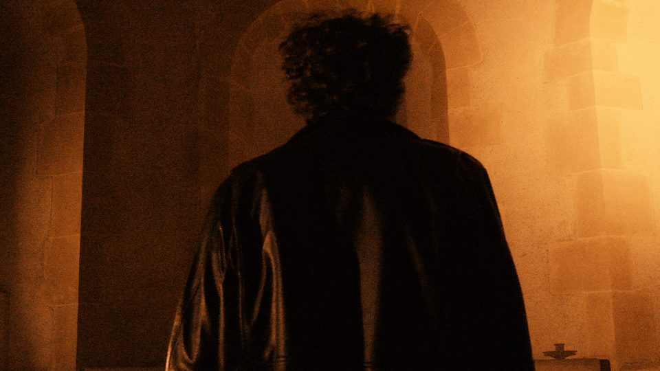 Figure in shadow beneath a stone archway in warm light